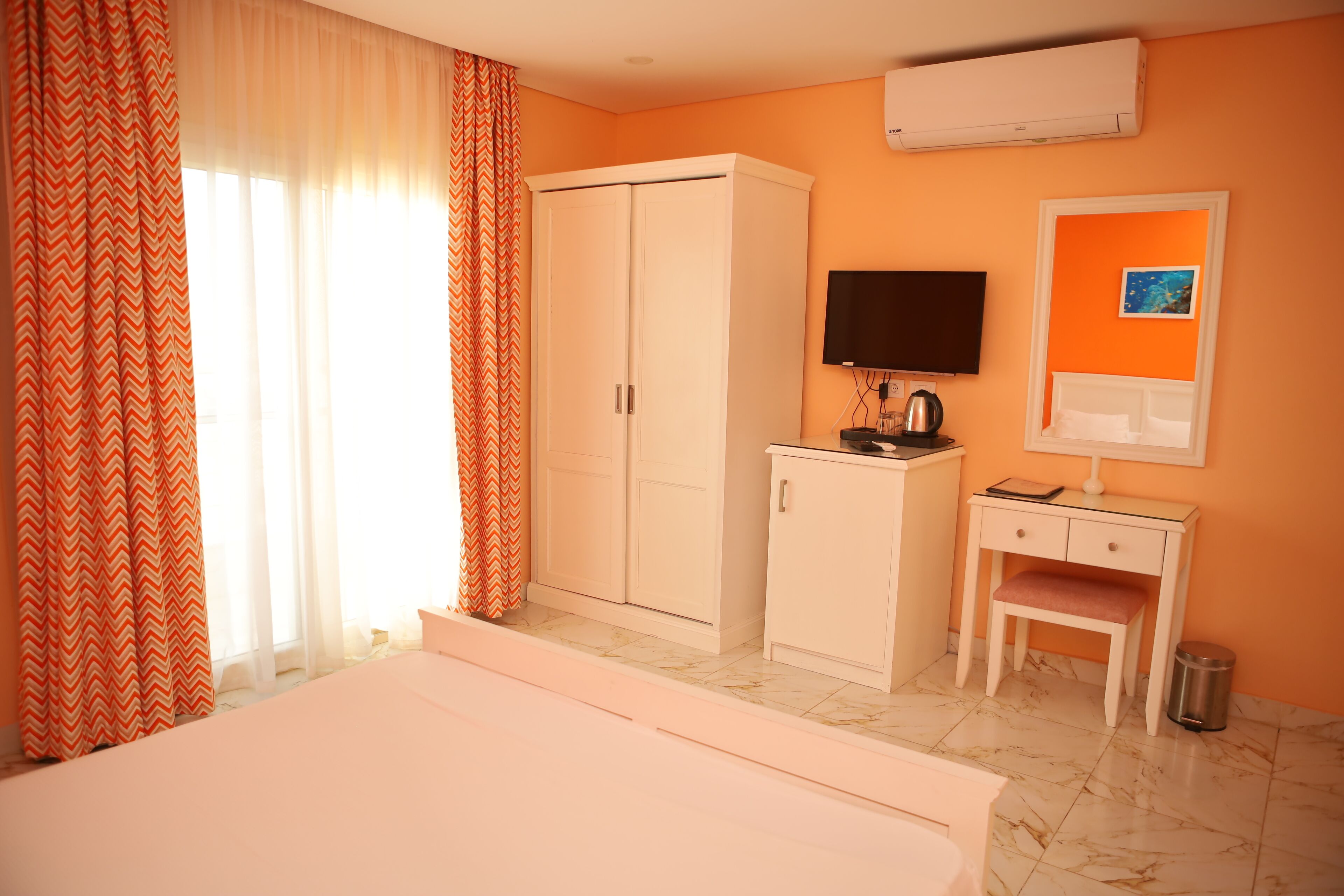 A hotel room with a bed, wardrobe, desk, chair, television, and a picture on the wall.