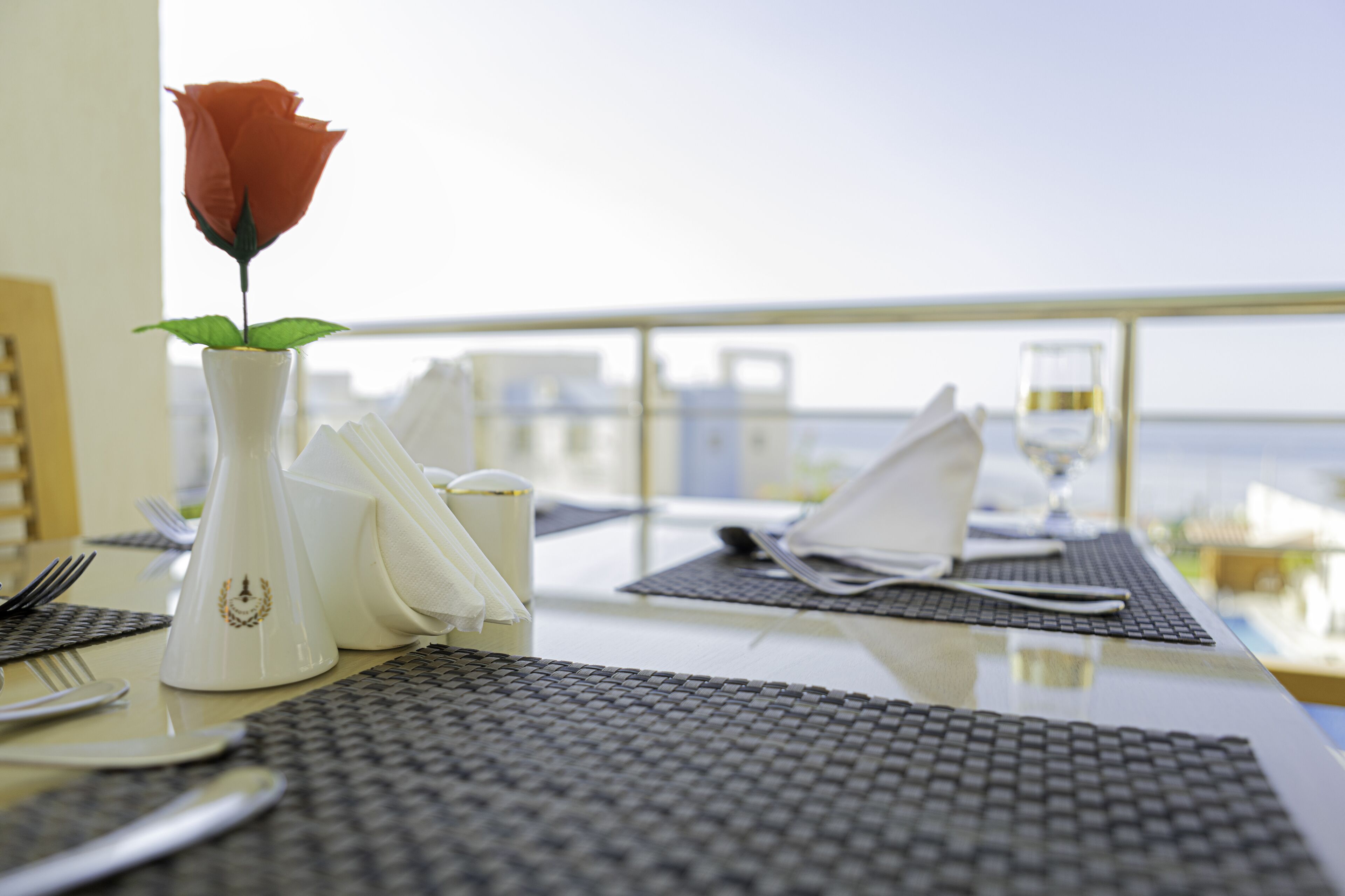Une table à manger avec une rose dans un vase, une serviette et un verre d’eau.