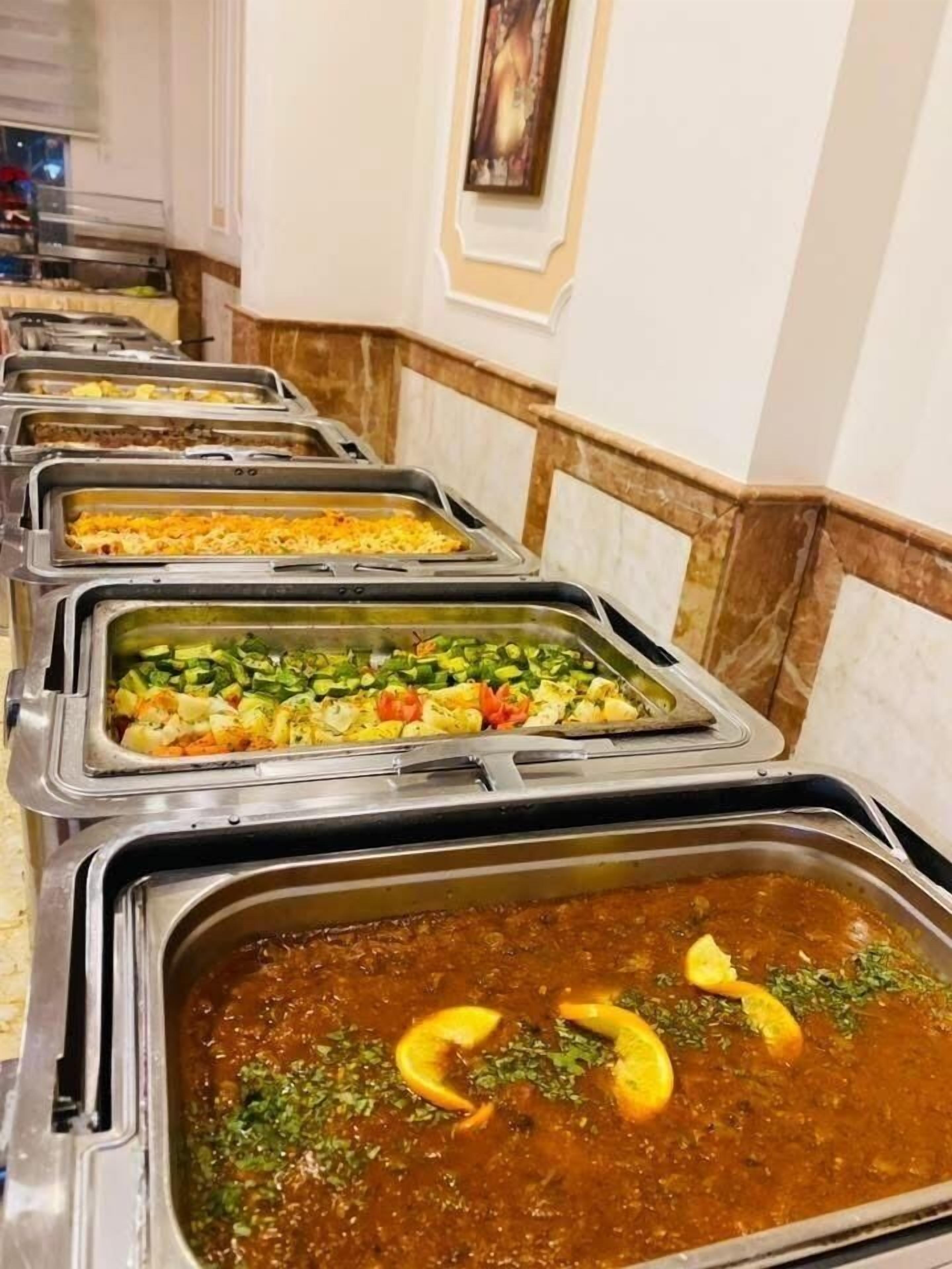 A buffet line with various dishes, including rice, vegetables, and a stew.