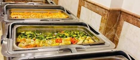 A buffet line with various dishes, including rice, vegetables, and a stew.