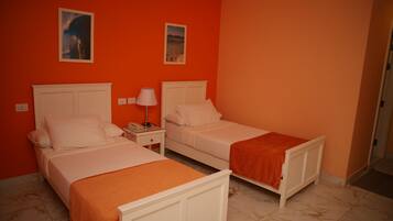 A room with two beds, each with white headboards and orange bedding. There are two bedside tables with lamps.