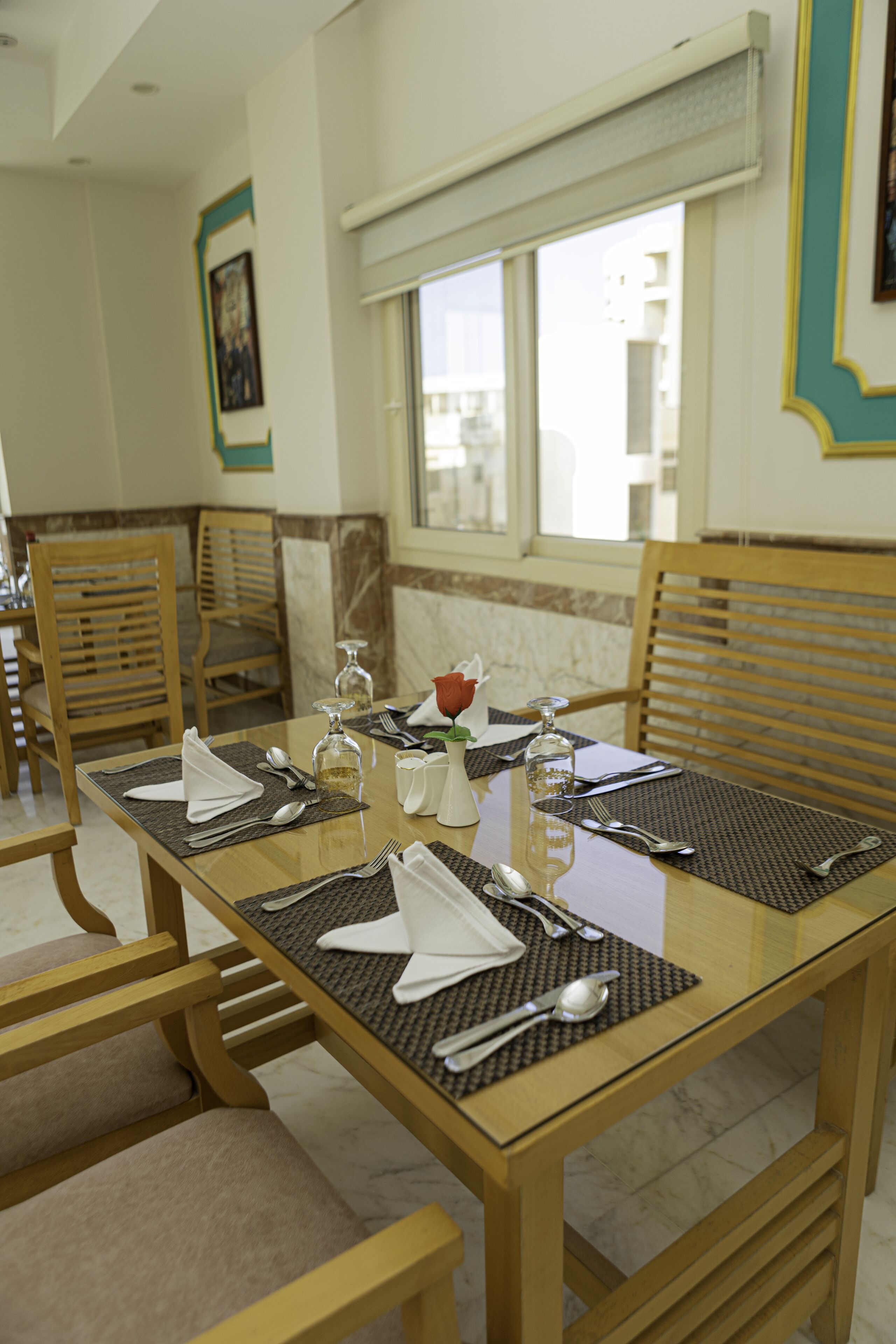 A dining table set with chairs, a vase with a flower, and a window with blinds.