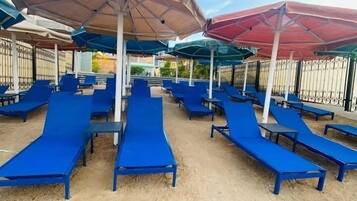 Ein Strandbereich mit blauen Liegestühlen und Sonnenschirmen, sandigem Untergrund und blauem Himmel.