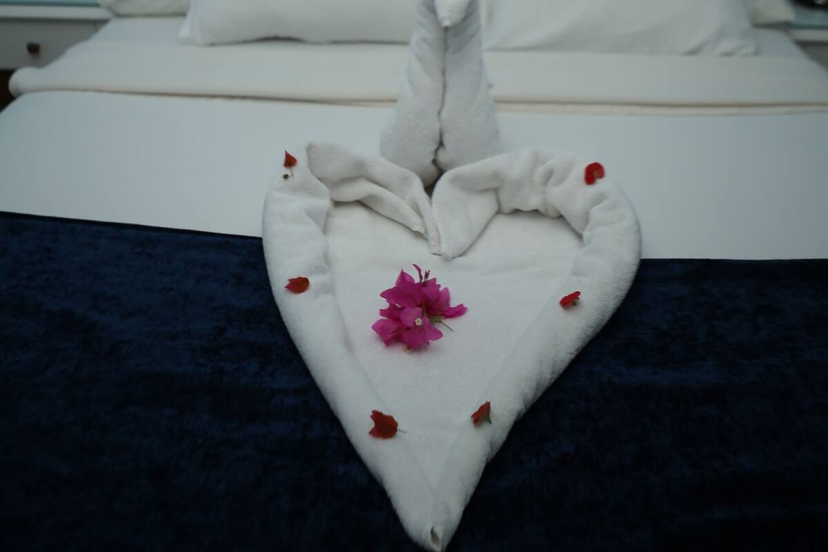 Ein ordentlich gemachtes Bett mit weißen Leinen und einer aufwendigen Handtuchskulptur auf der Bettdecke.