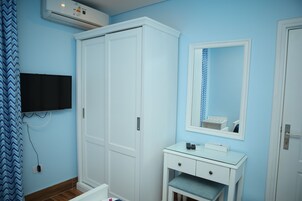A room with a wardrobe, a small vanity with a mirror, and a television mounted on the wall.