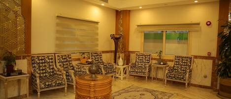 A spacious lobby with patterned armchairs, a central wooden table, and a large decorative rug.