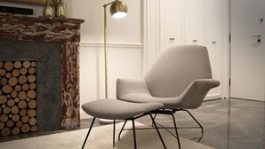 En modern stol med högt ryggstöd och metallben, placerad framför en öppen spis med en dekorativ överstycke och en hög golvlampa.
