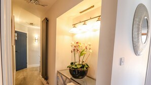 Un pasillo con una mesa consola de vidrio que sostiene una orquídea en maceta, un espejo montado en la pared y una lámpara.