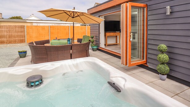 Un patio trasero con jacuzzi, mobiliario de mimbre y una puerta corrediza de vidrio que da a un área de patio.