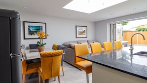Una cocina moderna con una isla central, taburetes de bar y una zona de comedor con sillas amarillas.