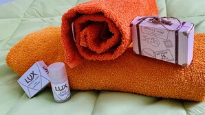 Een netjes gevouwen oranje handdoek, een klein flesje Lux 2in1 shampoo voor haar en lichaam, en een cadeauverpakking van Lux op een groene spreidek.
