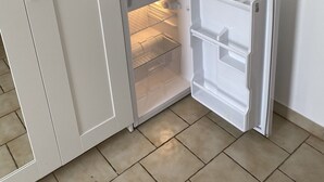Een compacte keuken met een ingebouwde magnetron, een kleine koelkast met vriesvak en een plank boven de magnetron.