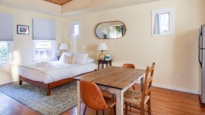 Een slaapkamer met een houten bed, een eettafel met stoelen, een spiegel en een koelkast.