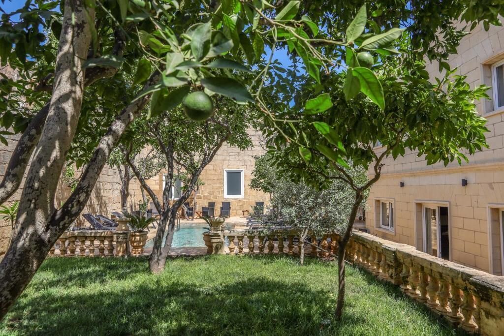 A courtyard with a swimming pool, stone walls, and a tree with green leaves.