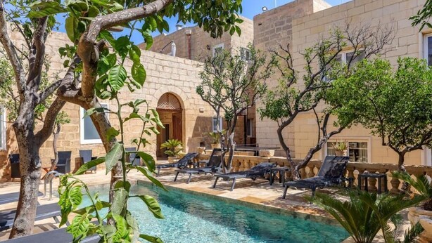 A poolside area with lounge chairs, a clear pool, and a building with stone walls and arched doorways. - Palazzo Pisani Malta Boutique & Spa (Zabbar)