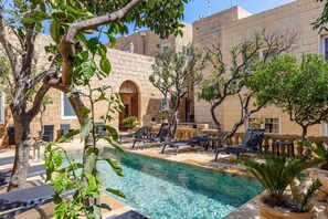 A poolside area with lounge chairs, a clear pool, and a building with stone walls and arched doorways. - Palazzo Pisani Malta Boutique & Spa (Zabbar)