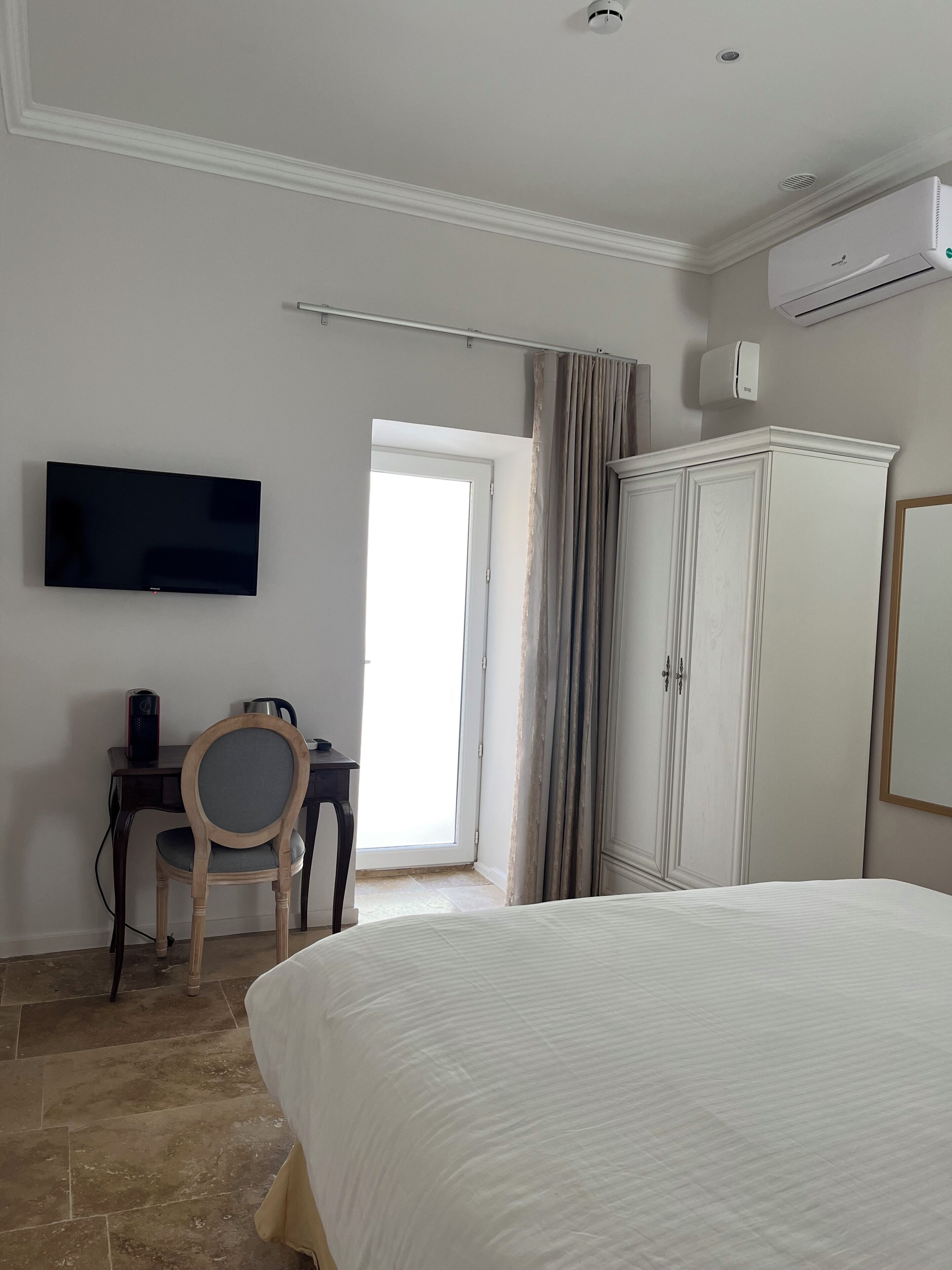 Ein Hotelzimmer mit Bett, Fernseher, Schreibtisch mit Stuhl, Kleiderschrank und Klimaanlage.
