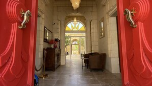 A grand entrance with red doors, a chandelier, and a view of a spacious interior with a staircase leading to a bright area. - Palazzo Pisani Malta Boutique & Spa (Zabbar)