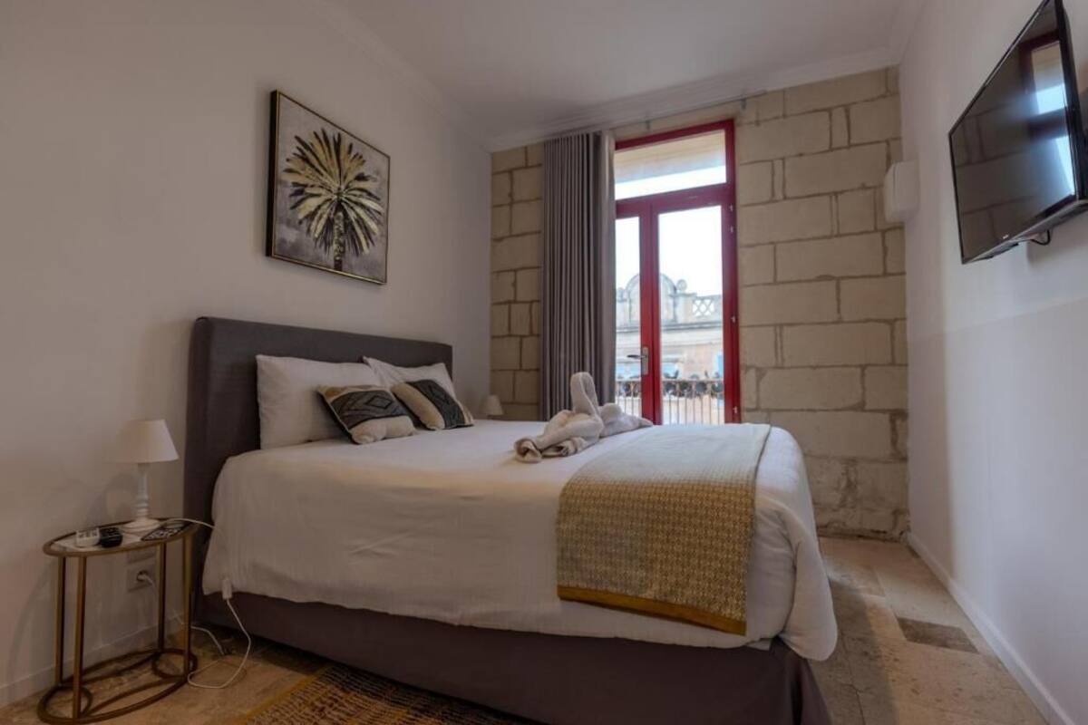 A hotel room with a bed, a TV mounted on the wall, and a window with a view of the outside.