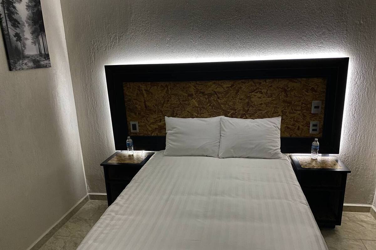 Habitación de hotel con una cama grande, dos mesitas de noche y un cabecero con diseño texturizado.