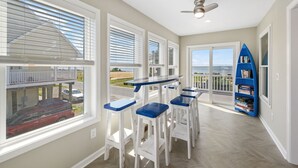 A balcony with white chairs and a blue table, overlooking a street with cars and a building.