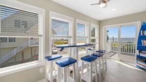 A balcony with a view of the sea, a ceiling fan, and a blue bar stool set.