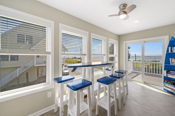 Un balcon avec vue sur la mer, un ventilateur de plafond et un ensemble de tabourets de bar bleus.