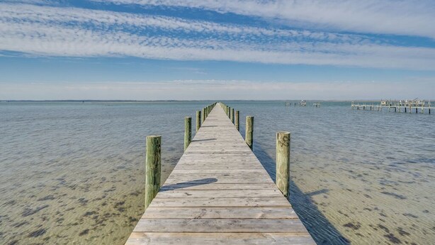 A wooden pier extending into calm waters under a clear sky.