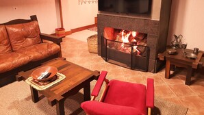Un salon chaleureux avec une cheminée, un canapé en cuir, une table basse en bois et un fauteuil rouge.