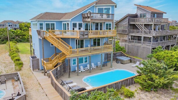 Une propriété en bord de mer, composée de plusieurs étages, dotée d’une piscine, d’un espace salon extérieur et d’une terrasse en bois.