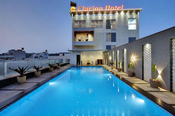 A hotel with a swimming pool, a modern building facade, and potted plants along the poolside.