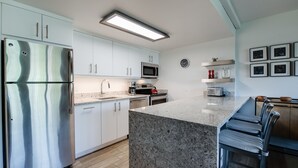 A modern kitchen with white cabinets, stainless steel appliances, a granite countertop, and a bar area with stools. - Trails End Mountainview Penthouse Condo: Ski In/Out, Stroll To Main Street (Breckenridge)