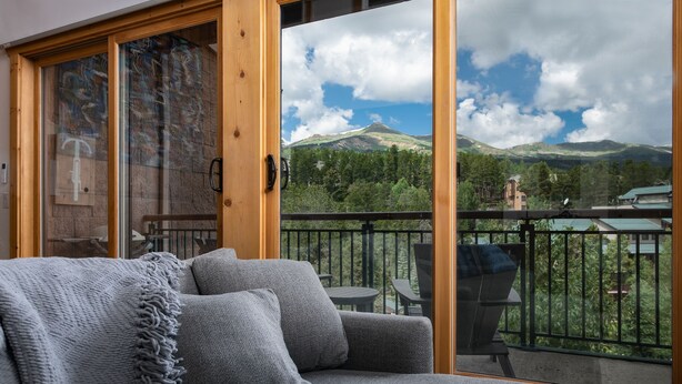 A balcony with a view of mountains, a sofa with a blanket, and a remote control on the floor. - Trails End Mountainview Penthouse Condo: Ski In/Out, Stroll To Main Street (Breckenridge)