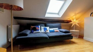 A cozy loft bedroom with a sloped ceiling, a skylight, a modern sofa, and a decorative floor lamp. - Le Wilson (Dijon)