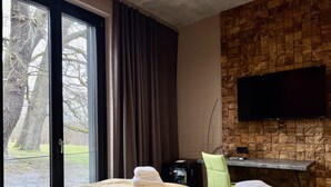 A hotel room with two beds, a TV mounted on a wooden wall, and a view of trees through a large window. - Zweirad Hotel Lenne (Schwerin)