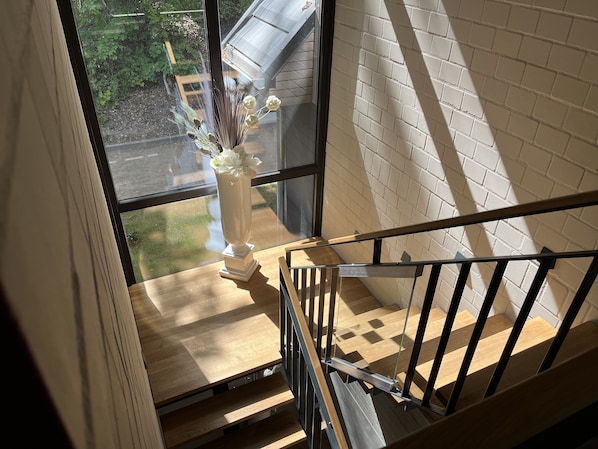 A wooden staircase with a white brick wall and a window overlooking a garden.