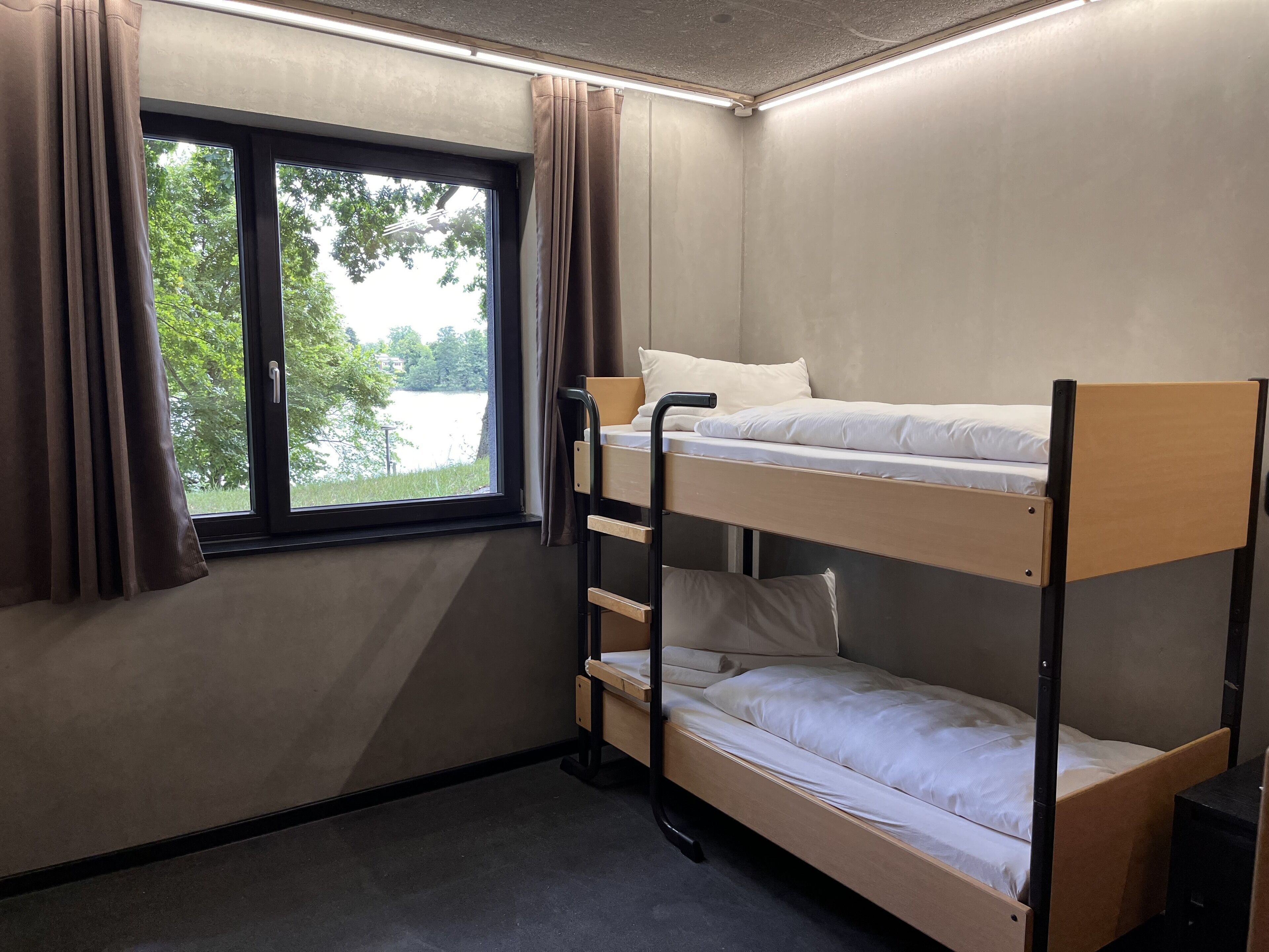 A bunk bed room with a window, curtains, and a view of greenery outside.