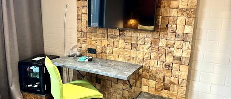 A compact room with a stone-patterned wall, a flat-screen TV mounted above a small table, a yellow chair, and a bench.