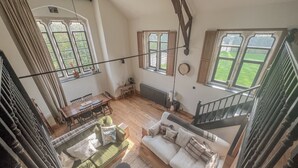 Amplia sala de estar con techo alto, vigas de madera, una escalera y grandes ventanales con vistas al exterior.