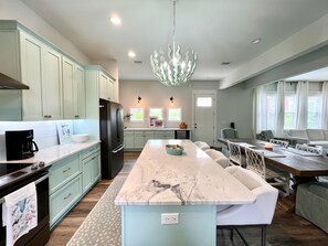 A modern kitchen with light blue cabinets, a large island, and a chandelier. - North Cape, Private Pool (April26)Gulf View home, pet friendly, VayK Gear! (Port Saint Joe)