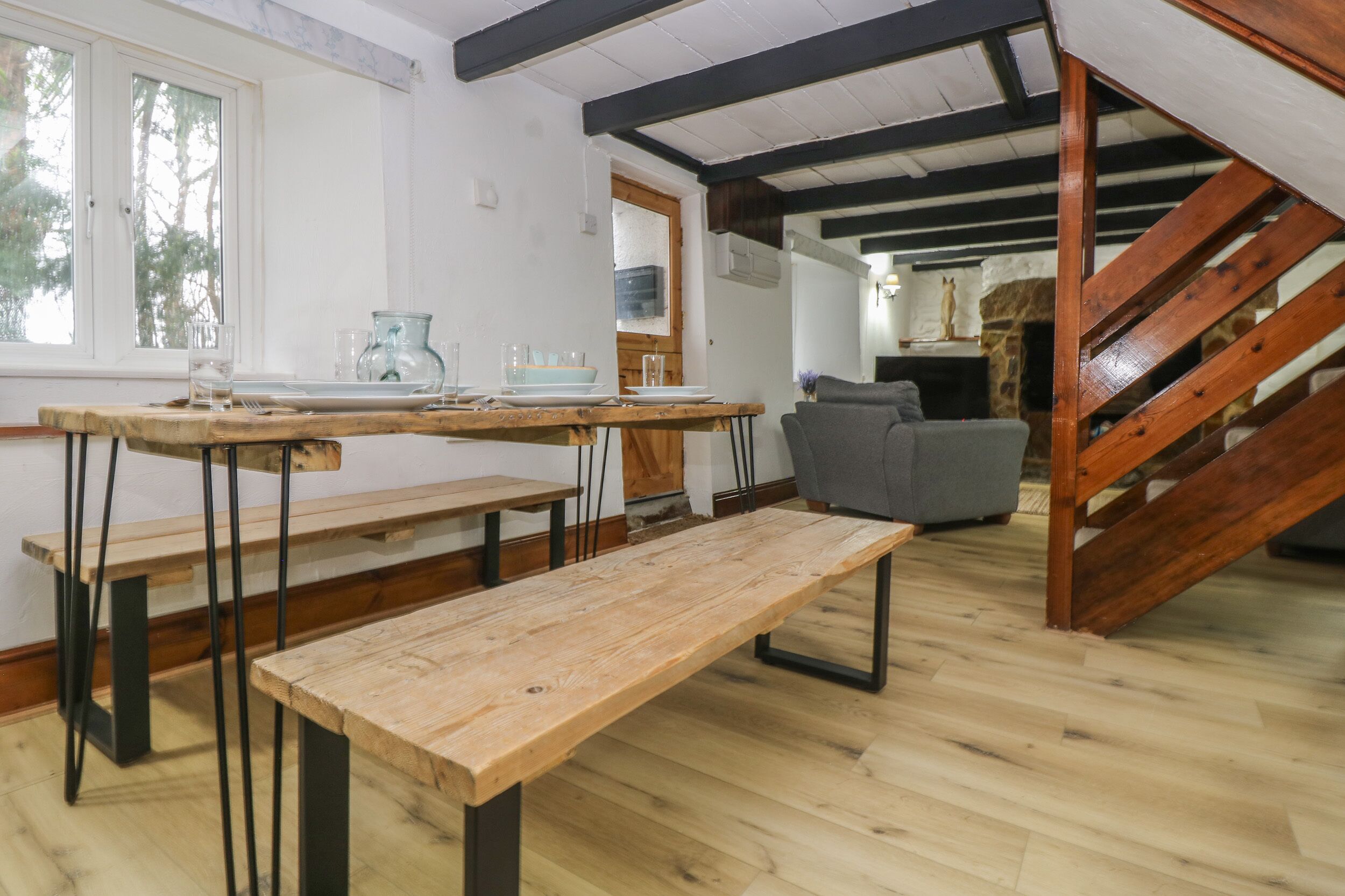 A room with a wooden floor, a wooden bench, a table with plates and glasses, a grey sofa, and a staircase.
