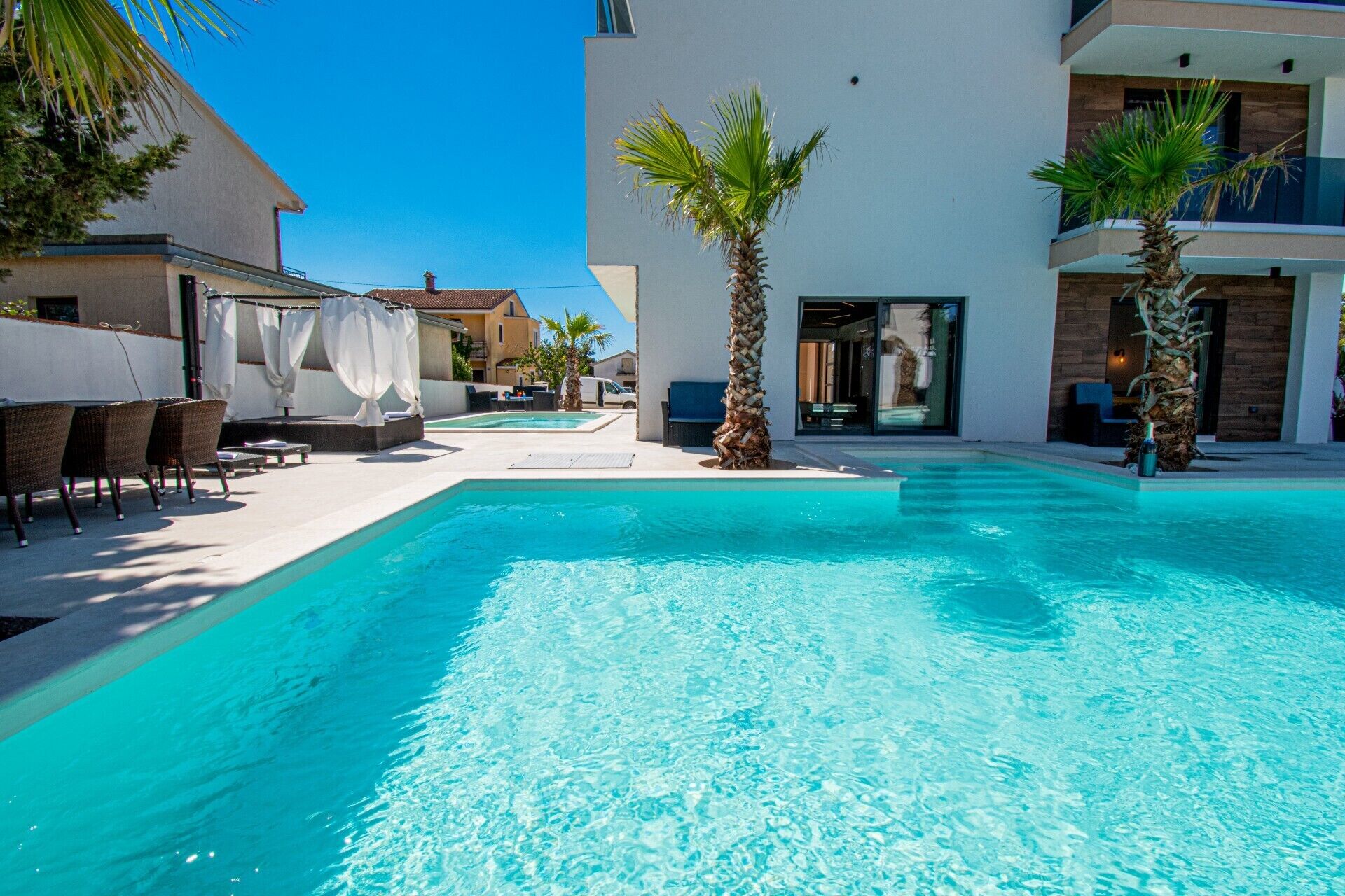 A swimming pool with lounge chairs and palm trees, surrounded by modern buildings.