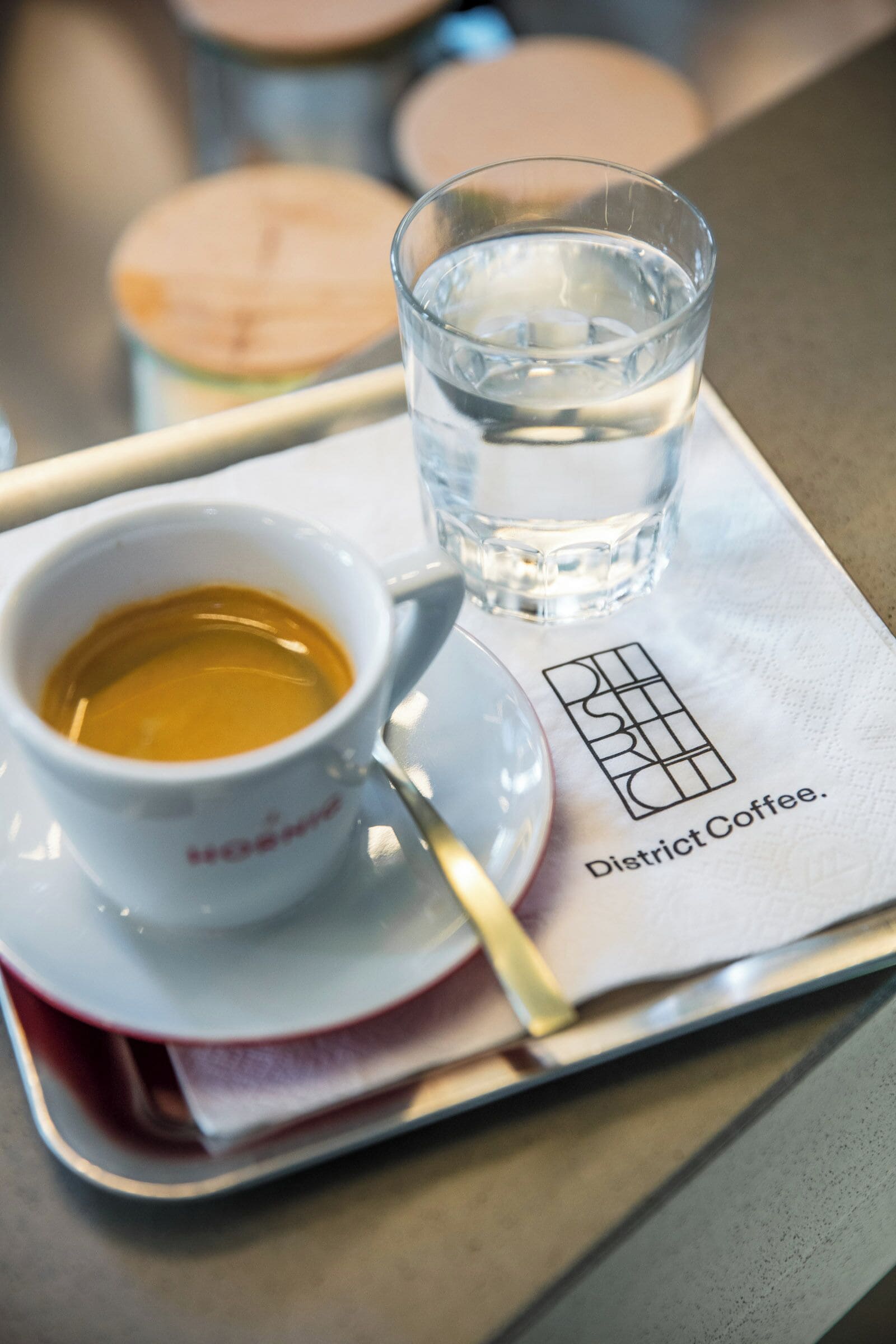 Bandeja con una taza de café y un vaso de agua sobre una servilleta con el texto 'District Coffee'.