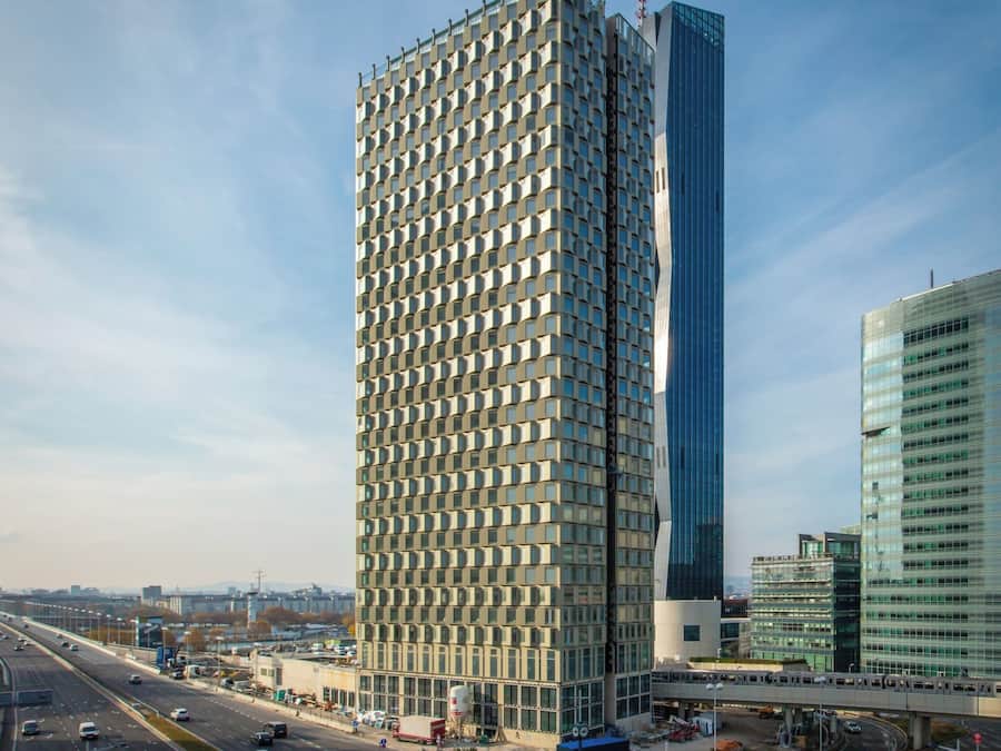 Un edificio moderno de gran altura con fachada de entramado y una destacada torre de cristal.