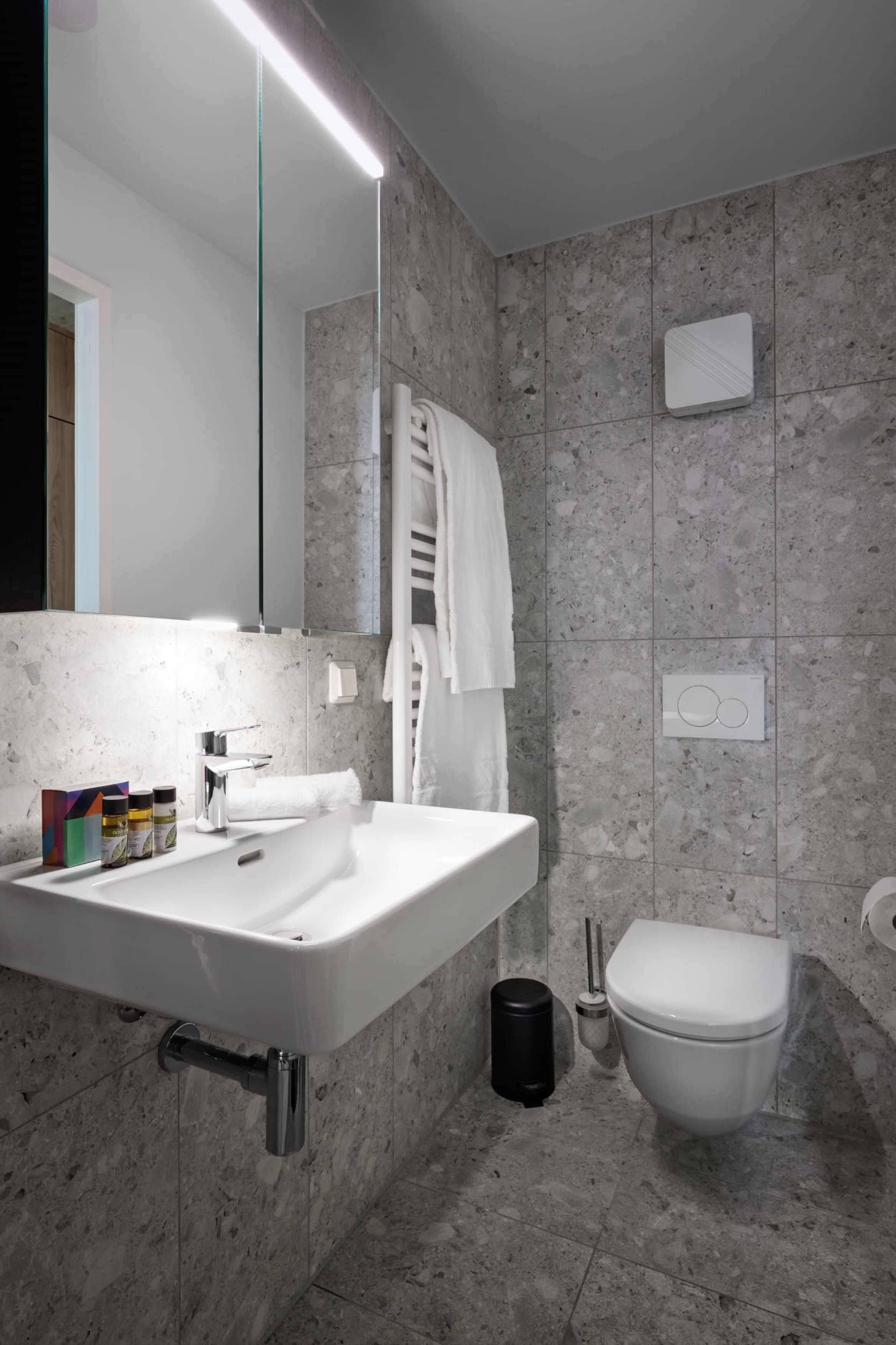 Un baño moderno con lavamanos, espejo y retrete blancos.