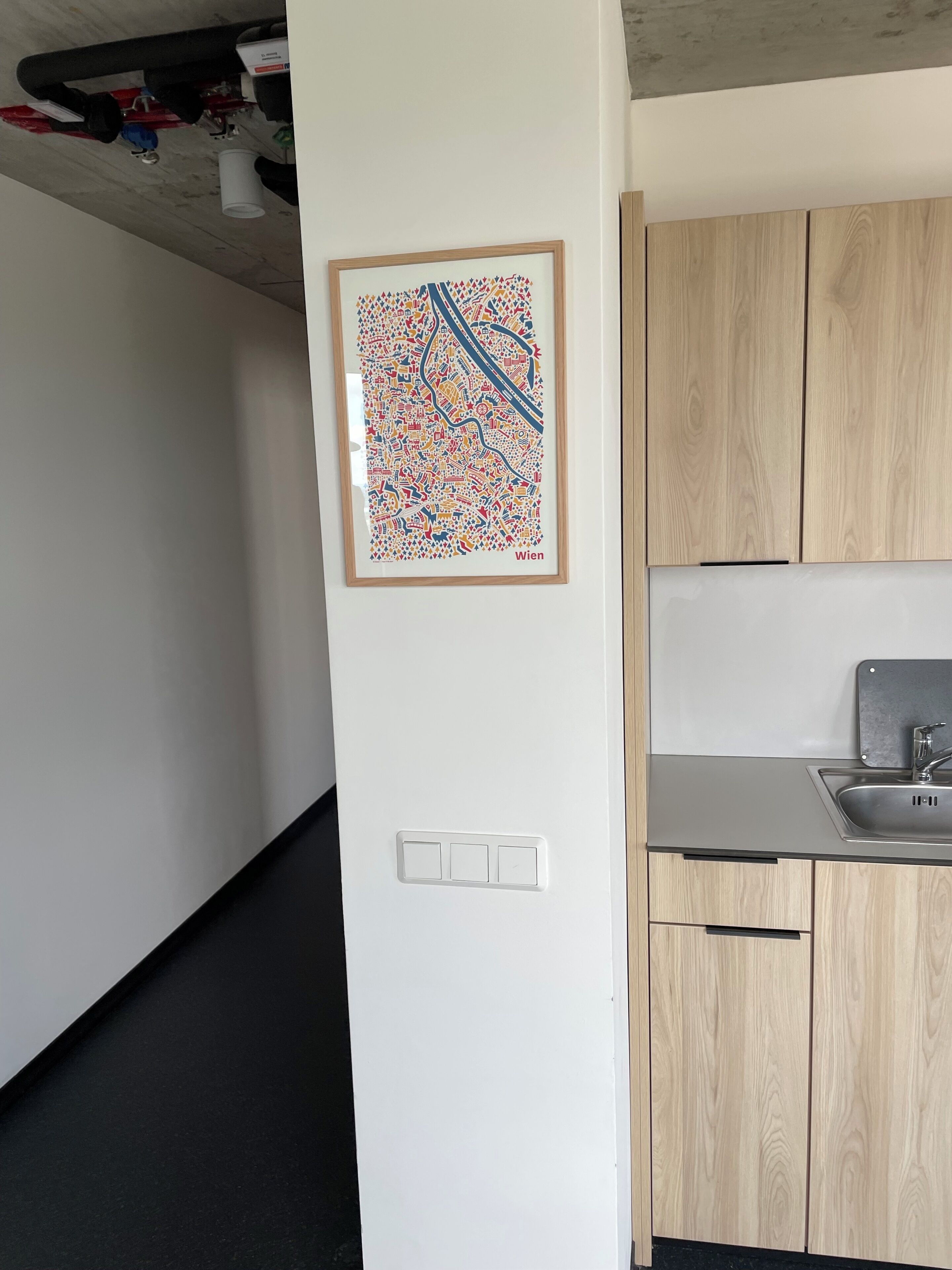 A modern kitchen with wooden cabinets, a stainless steel sink, and a framed city map on the wall.