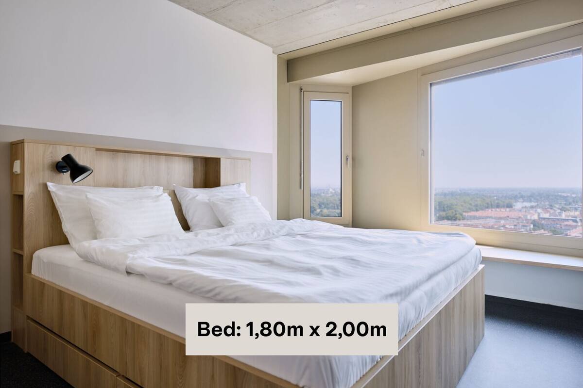 A modern bedroom with a bed measuring 1.80m x 2.00m, large windows, and a city view.