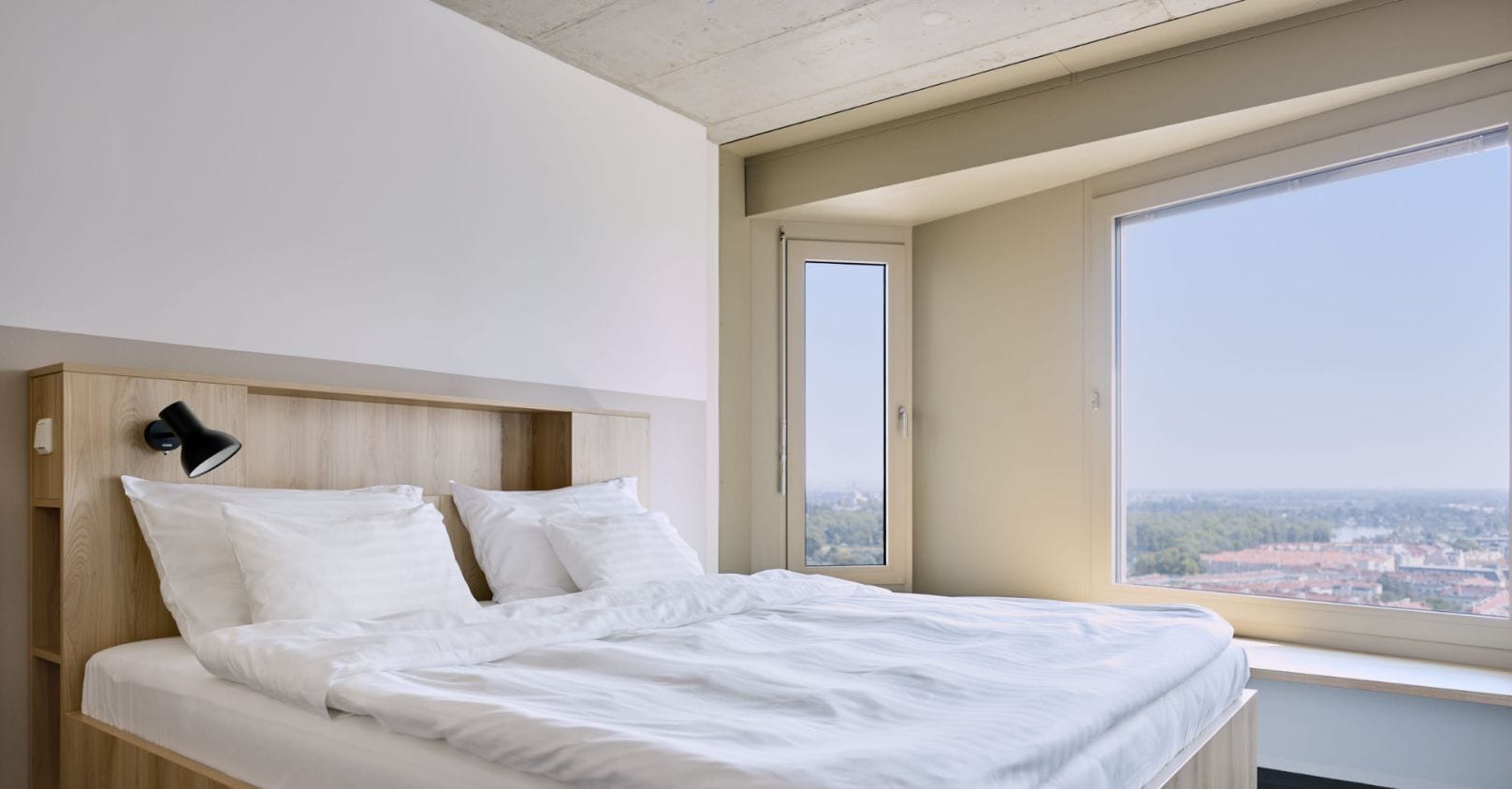 A modern bedroom with a bed measuring 1.80m x 2.00m, large windows, and a city view.