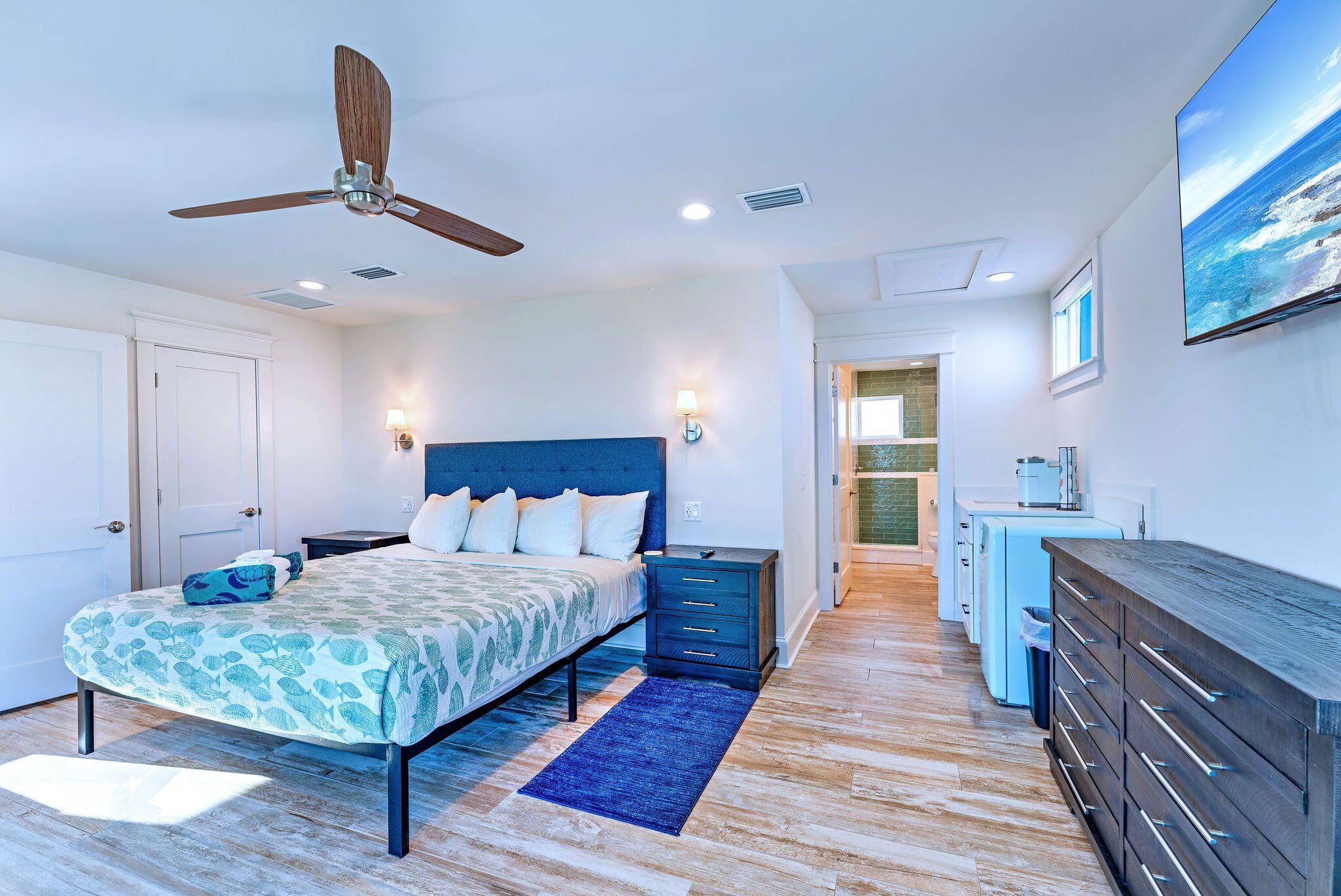 A bedroom with a bed, bedside tables, a ceiling fan, and a view of the kitchen.