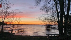 A lakeside picnic area with benches and a flag, surrounded by trees. - Hydrus cozy 2 bedroom cottage (Kawartha Lakes)